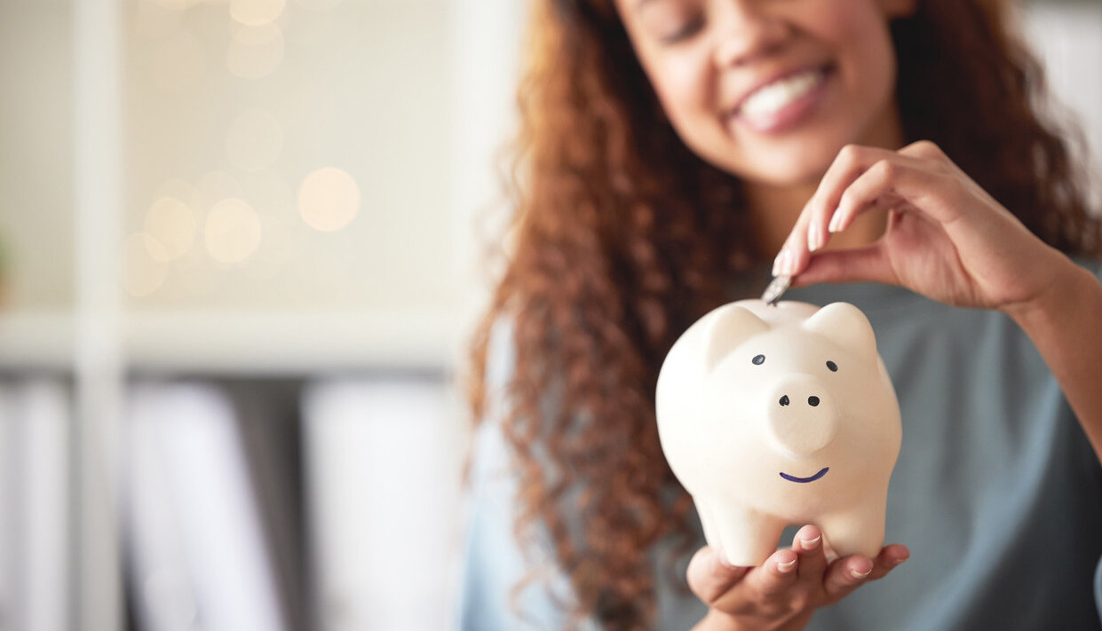 Eine glückliche junge Frau, die ein Sparschwein hält und eine Münze als Ersparnisse hinterlegt.  | © © iStock.com | PeopleImages