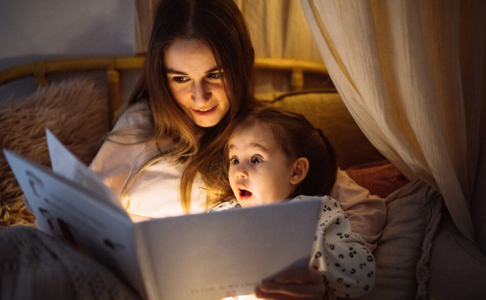 Die junge, liebevolle Mutter liest ihrer kleinen schönen Tochter, die in ihrem Bett schlafen geht, Gutenachtgeschichten vor. | © © iStock.com | ozgurcankaya