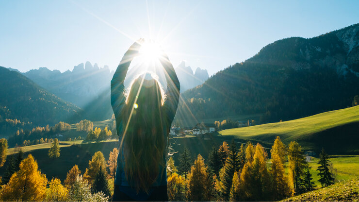 Frau greift nach der Sonne mit Blick auf Tal und Berge | © Ascent/PKS Media Inc./Stone via Getty Images