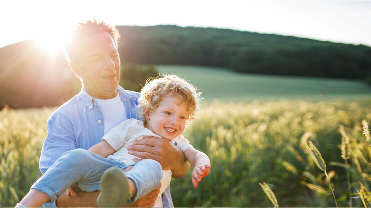 Ein alter Großvater mit seinem kleinen Enkel auf einer Wiese, der Spaß hat. | © Halfpoint Images/Moment via Getty Images