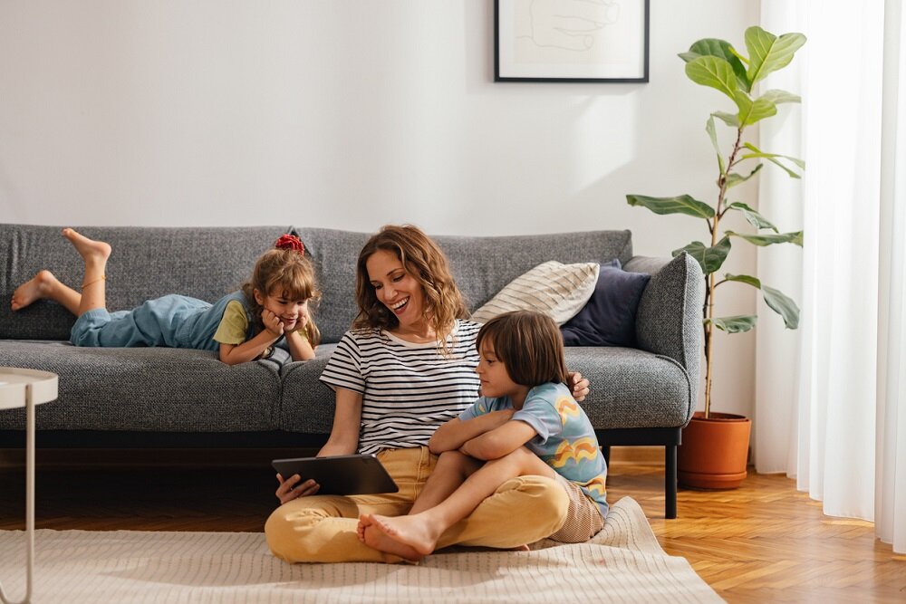 Die Mutter sitzt auf dem Boden und schaut sich mit ihren Kindern etwas auf dem digitalen Tablet an | © © iStock.com | miniseries